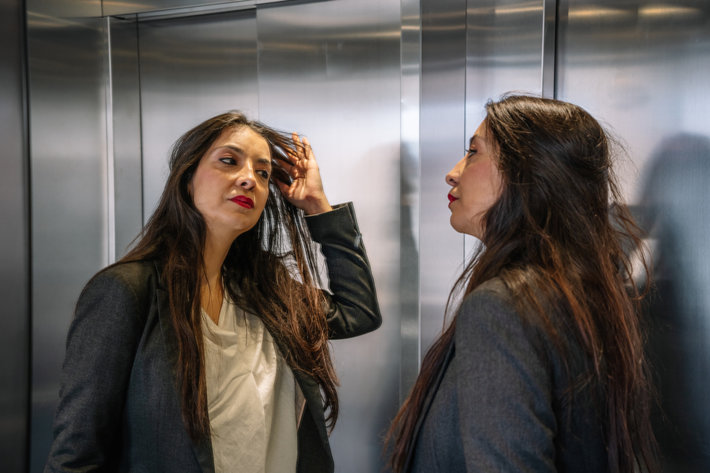 Business woman addict looking at an elevator mirror 